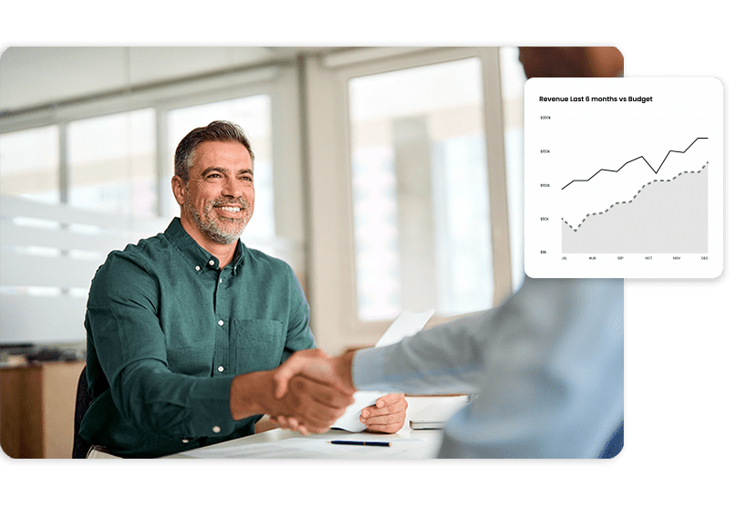 individual-prep A man in a green shirt smiles and shakes hands with someone across a desk. There is a graph in the image showing an upward trend.